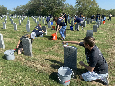 Two volunteers cleaning headstones and using brushes and buckets of water.