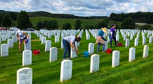 Four volunteers cleaning headstones in a national cemetery for the National Day of Service.